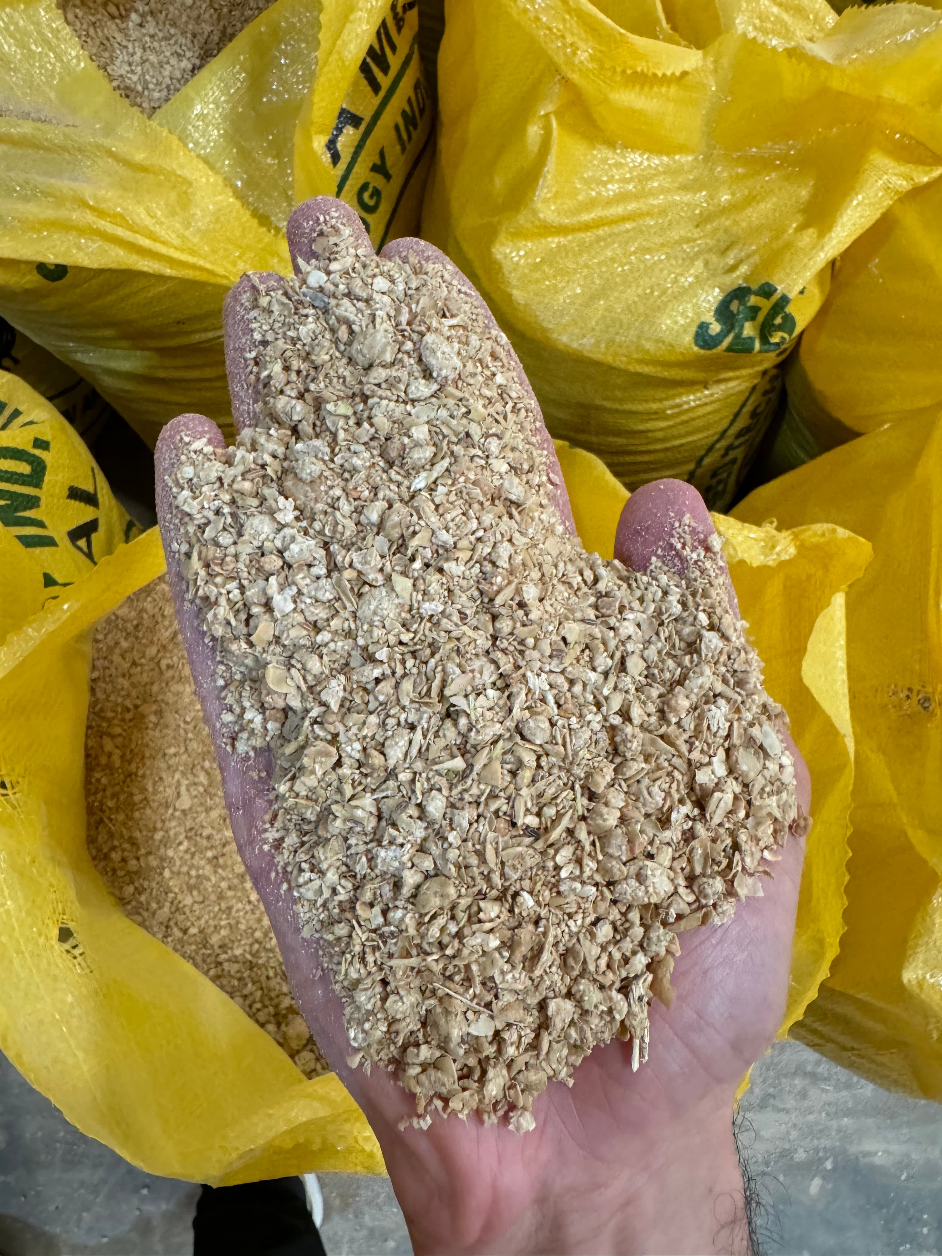 Soybean meal from Seed Technology Industry — held in hand with yellow Chicken and Fish brand sacks behind